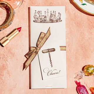 A notepad with a illustration of a cocktail glass and a corkscrew on the cover, placed on a table with various objects around it.