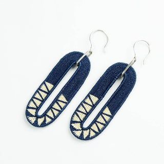 A pair of handmade geometric dangle earrings made from dark blue woven fabric with cream-colored triangular patterns, attached to silver fishhook wires, shown on a plain white background.