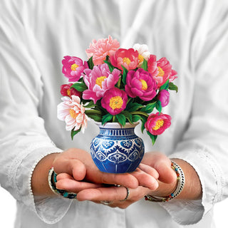 Person holding a vase with colorful flowers against a white background