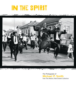 Black and white cover image of a book titled 'In the Spirit: The Photography of Michael P. Smith' showing a photograph of people dancing and enjoying a celebration in the street.