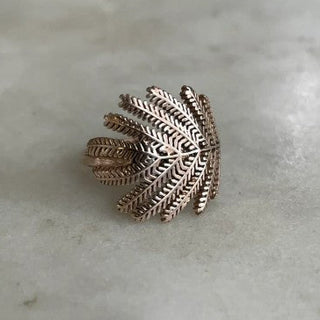 A textured metallic ring with a leaf or fern-like openwork design, shown on a light gray stone surface.