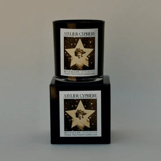 A black glass jar candle with a vintage-style label featuring a star and the brand name Adler Cyprière, displayed on top of a matching black rectangular box against a neutral gray background.