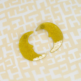 A pair of gold crescent moon-shaped earrings with a textured, displayed on a light beige background with a white geometric maze pattern.