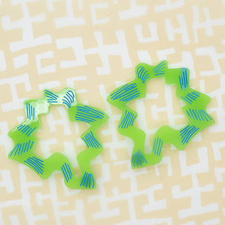 Two lime green wavy ring-shaped earrings with blue striped accents, displayed on a light beige background with a white maze pattern.